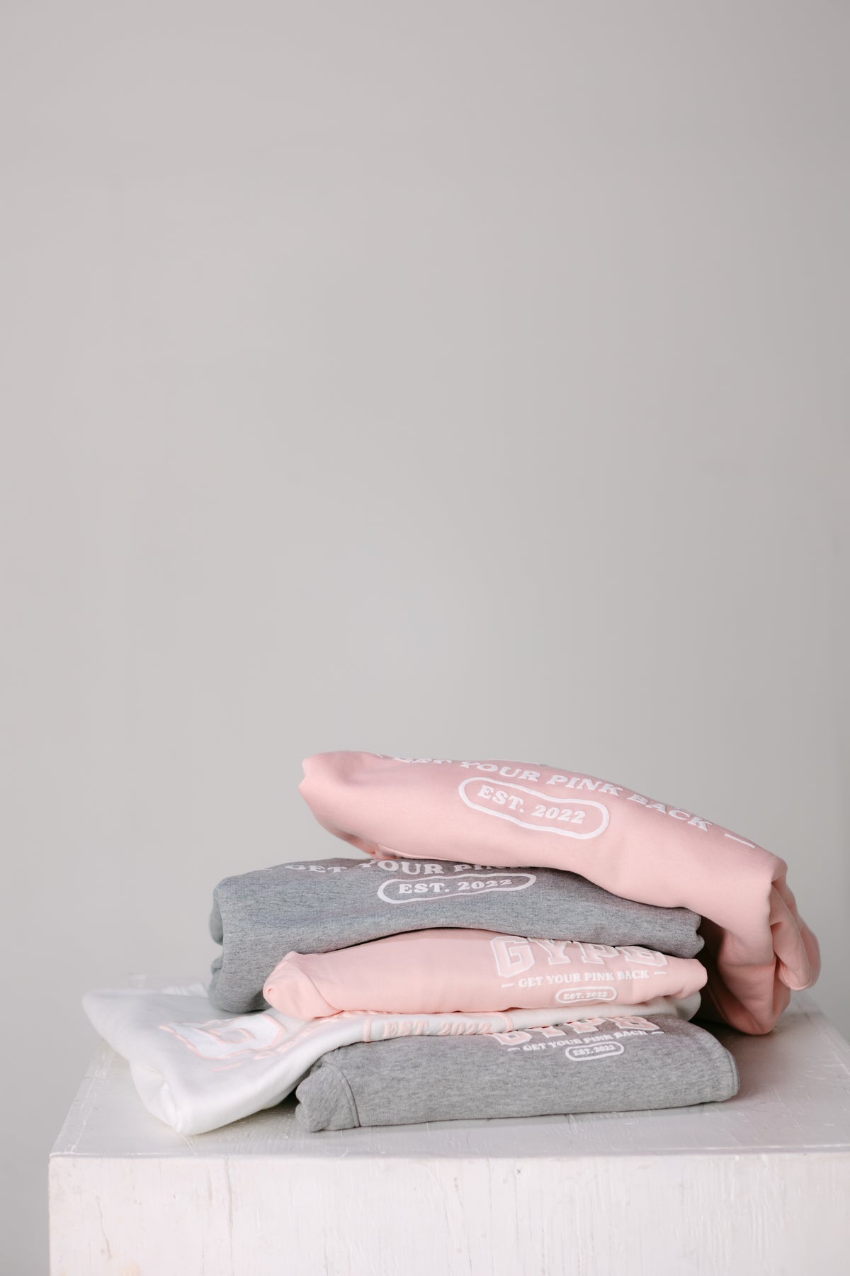 Folded GYPB sweatshirts stacked on a white block